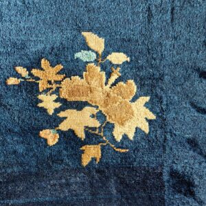 Textured navy blue rug features a tan floral pattern with minor light blue accents and a beige border.