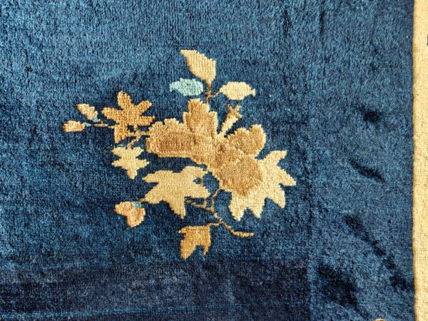 Textured navy blue rug features a tan floral pattern with minor light blue accents and a beige border.