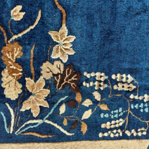 A textured, deep blue rug corner showing a beige floral design and wide tan border.