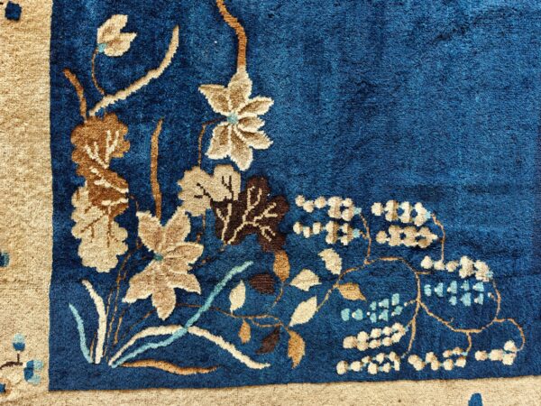 A textured, deep blue rug corner showing a beige floral design and wide tan border.