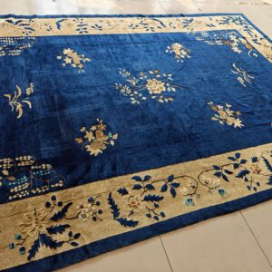 A large, deep blue rug featuring scattered floral designs and a wide tan decorative border on light tile.