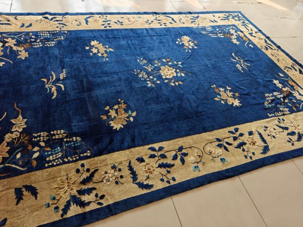 A large, deep blue rug featuring scattered floral designs and a wide tan decorative border on light tile.