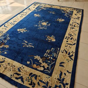 Royal blue rug with a gold border and intricate floral pattern on light tile flooring.
