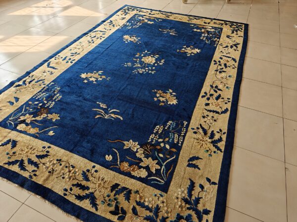 Royal blue rug with a gold border and intricate floral pattern on light tile flooring.