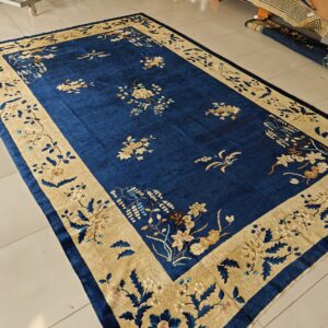 Deep blue floral rug featuring a wide tan border is displayed on light beige square tile flooring.