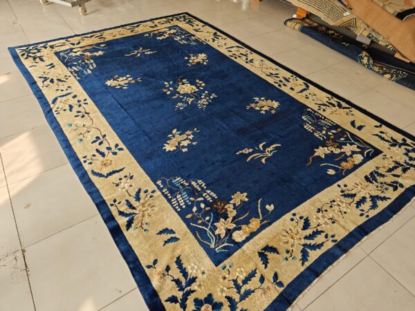 Deep blue floral rug featuring a wide tan border is displayed on light beige square tile flooring.