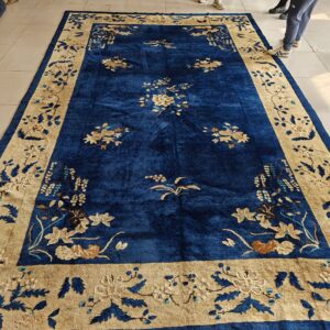 Deep blue rug with a wide beige floral border displayed flat on a light tiled floor.