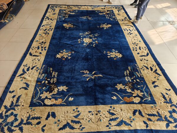Deep blue rug with a wide beige floral border displayed flat on a light tiled floor.