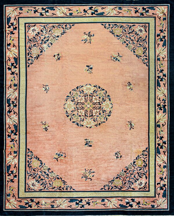 Low-pile pink rug with navy blue floral borders and a round central floral medallion.