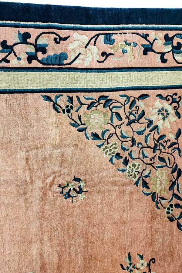 Close-up of a rug corner showing a salmon pink field and navy, teal, and sage borders with floral patterns.