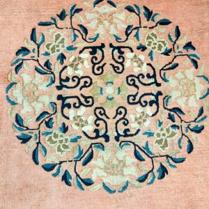 Peach rug surface showing a circular medallion with detailed teal, ivory, and beige botanical motifs.