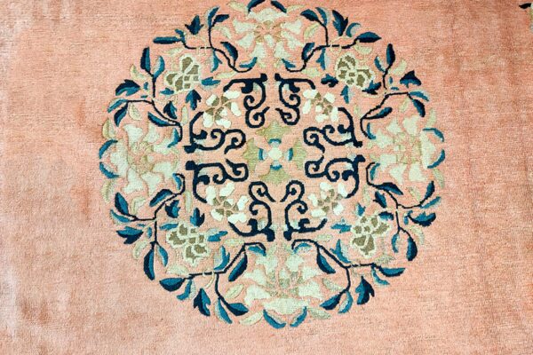 Peach rug surface showing a circular medallion with detailed teal, ivory, and beige botanical motifs.