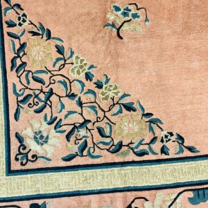 Close-up of a peach rug featuring teal and cream floral patterns and a khaki geometric border.