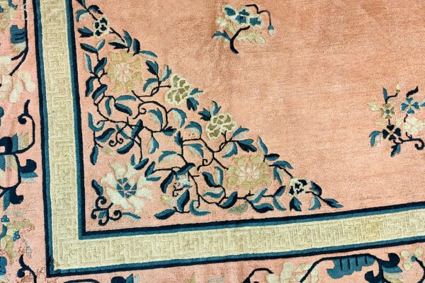 Close-up of a peach rug featuring teal and cream floral patterns and a khaki geometric border.