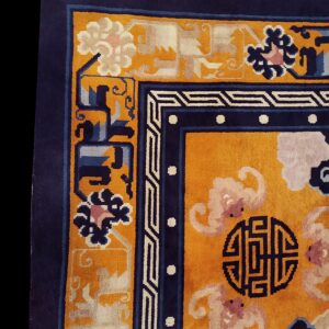 Close-up shows a plush yellow rug corner with a navy blue border and stylized floral and geometric patterns.