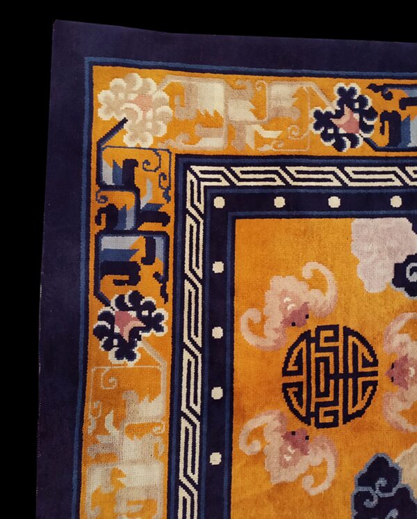 Close-up shows a plush yellow rug corner with a navy blue border and stylized floral and geometric patterns.