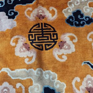 Textured, orange rug featuring pink, beige, and dark blue cloud patterns and a central black circular symbol.