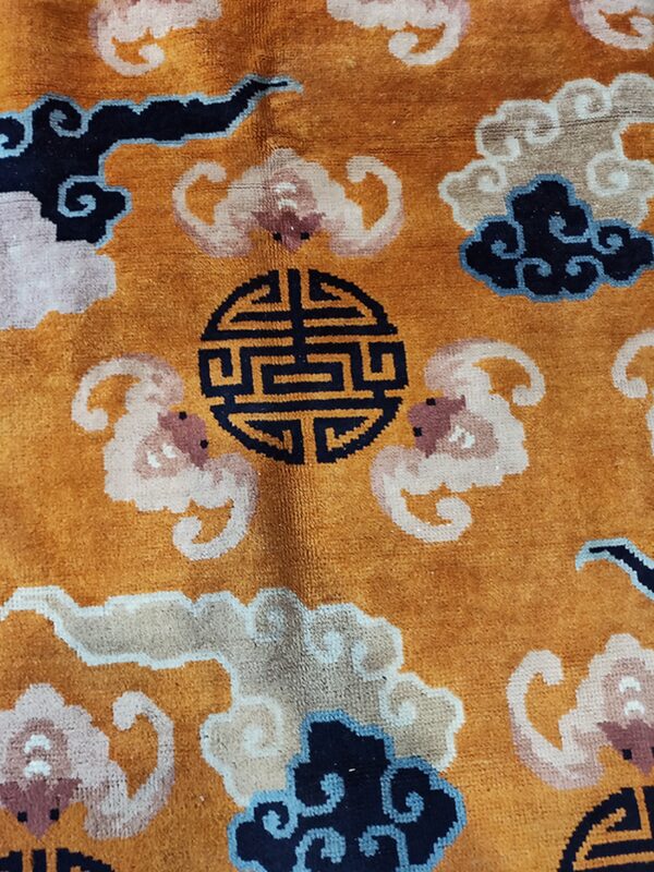 Textured, orange rug featuring pink, beige, and dark blue cloud patterns and a central black circular symbol.