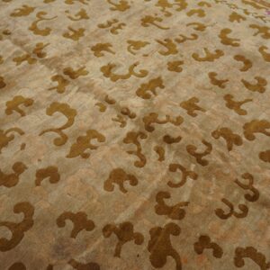 Tan rug with scattered bronze stylized cloud patterns and a visible pink accent border detail.