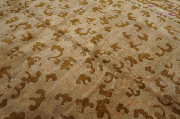 Tan rug with scattered bronze stylized cloud patterns and a visible pink accent border detail.