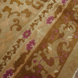 Medium-pile rug detail in tan and brown with ornate magenta floral patterns on distressed wood flooring.