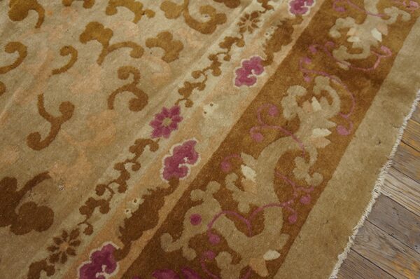 Medium-pile rug detail in tan and brown with ornate magenta floral patterns on distressed wood flooring.