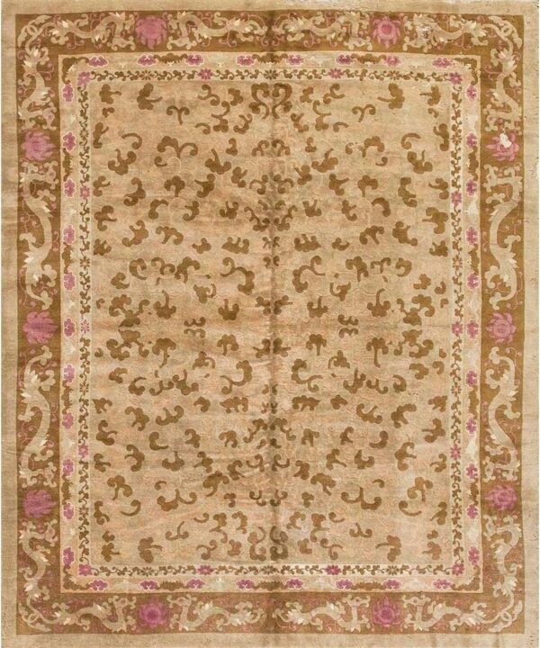 Low-pile tan rug with contrasting brown scrolling motifs and borders accented by bright pink floral designs.