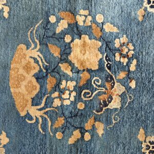 Muted blue low-pile rug with large circular tan and dark blue stylized floral designs.