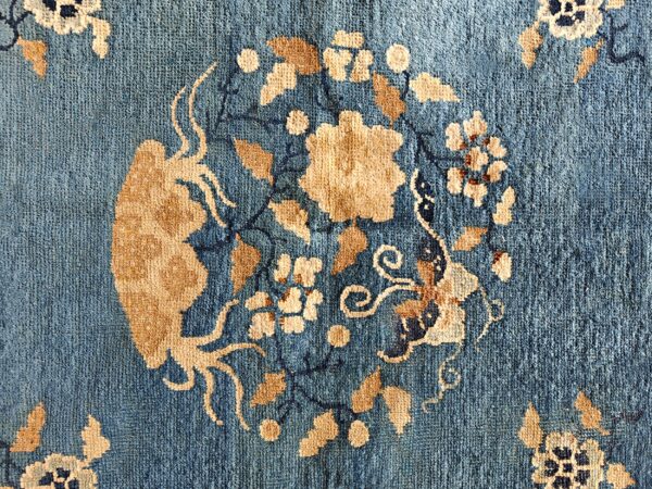 Muted blue low-pile rug with large circular tan and dark blue stylized floral designs.