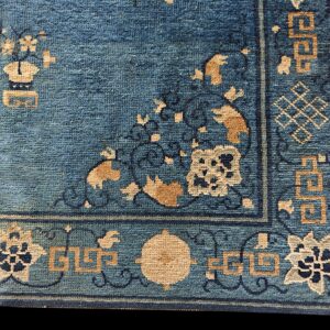 A corner detail of a blue rug featuring tan and dark blue floral and geometric motifs.