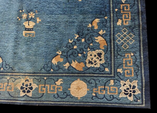 A corner detail of a blue rug featuring tan and dark blue floral and geometric motifs.
