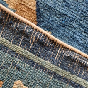 Close-up shows a bound edge dividing blue geometric low pile from a dense dark blue shaggy texture.