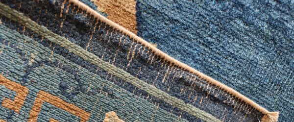 Close-up shows a bound edge dividing blue geometric low pile from a dense dark blue shaggy texture.
