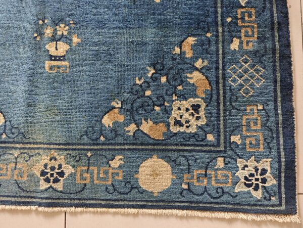Closeup of a faded blue short pile rug corner with tan geometric and floral border designs.