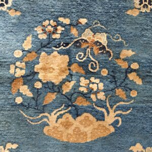 Muted teal blue rug with a low pile featuring a large central floral arrangement in tan and cream colors.