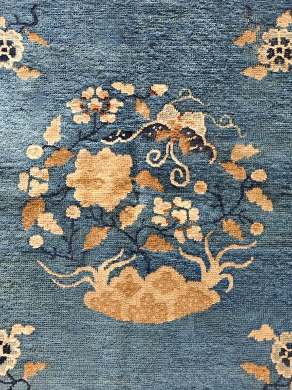 Muted teal blue rug with a low pile featuring a large central floral arrangement in tan and cream colors.