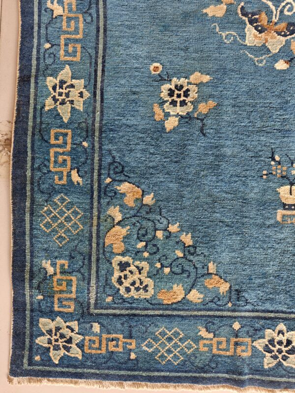 Teal blue rug corner with multi-band border and geometric meander patterns in tan and ivory.