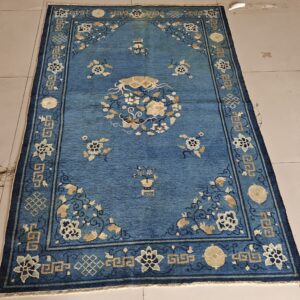 Low-pile blue rug featuring tan and cream floral patterns and geometric borders on light tiled flooring.