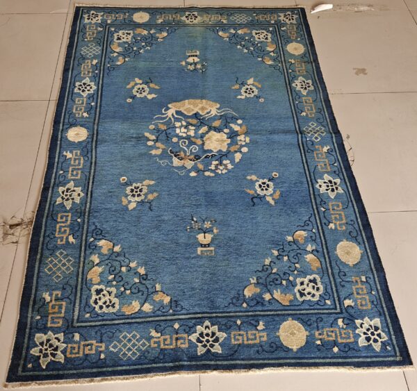 Low-pile blue rug featuring tan and cream floral patterns and geometric borders on light tiled flooring.