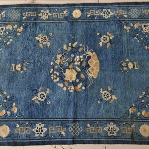 Textured blue rug with gold and navy floral patterns and a complex geometric border on light tile flooring.