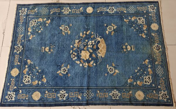Textured blue rug with gold and navy floral patterns and a complex geometric border on light tile flooring.