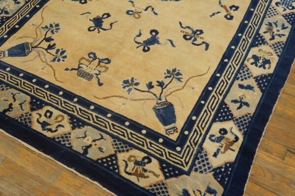 Low-pile rug with tan field, dark blue border, and scattered vases on wood plank flooring.