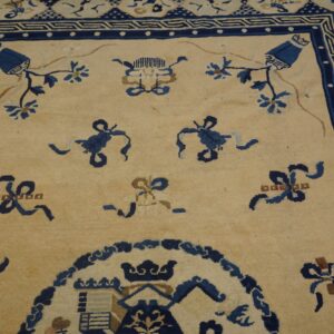 Beige rug field with scattered blue floral and ribbon motifs and an elaborate navy border.