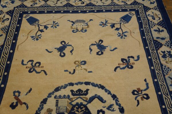 Beige rug field with scattered blue floral and ribbon motifs and an elaborate navy border.
