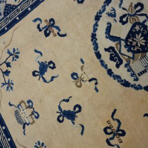 Ivory rug with indigo floral sprays, ribbon knots, and a detailed traditional blue border on wood floor.