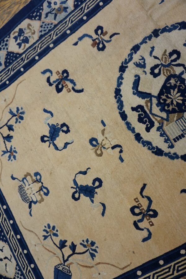 Ivory rug with indigo floral sprays, ribbon knots, and a detailed traditional blue border on wood floor.