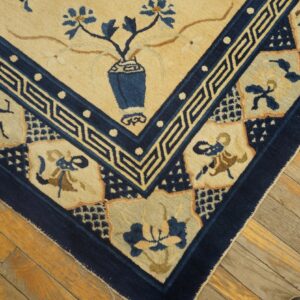 Close-up of a tan and navy rug corner with stylized floral motifs resting on distressed wooden plank flooring.
