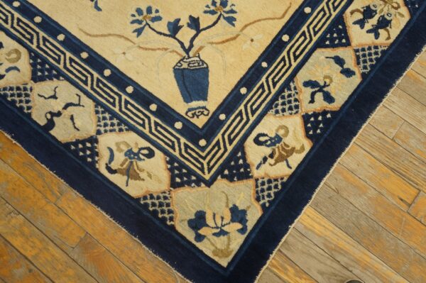 Close-up of a tan and navy rug corner with stylized floral motifs resting on distressed wooden plank flooring.
