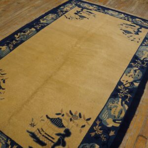 Golden yellow high-pile rug with a wide navy and teal scenic border rests on worn wood plank flooring.