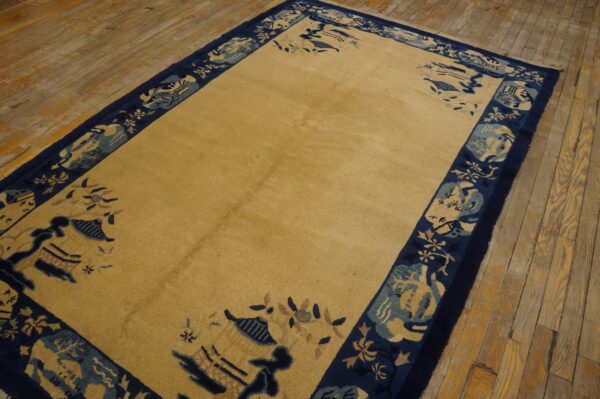 Golden yellow high-pile rug with a wide navy and teal scenic border rests on worn wood plank flooring.